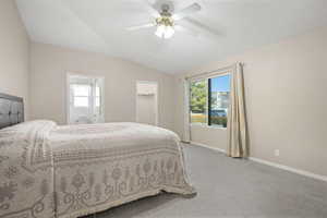 Carpeted bedroom with vaulted ceiling, multiple windows, a spacious closet, ceiling fan, and connected bathroom