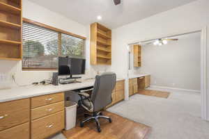 Home office with built in study area, ceiling fan, and light carpet