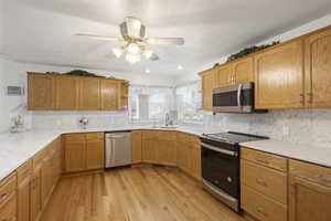 Kitchen with stainless steel appliances, light wood-style floors, light stone counters, a ceiling fan, and decorative backsplash
