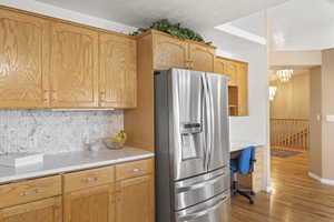 Kitchen with stainless steel refrigerator with ice dispenser, light wood-type flooring, backsplash, a chandelier, and a desk