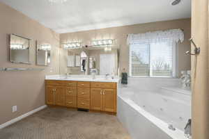 Bathroom featuring double vanity, a jetted tub, and light carpet