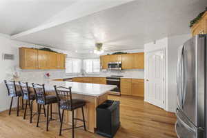 Kitchen with stainless steel appliances, backsplash, a peninsula, light wood-style floors, and ceiling fan