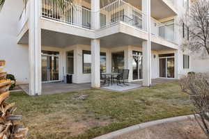 Rear view of property featuring a patio area, stucco siding, a lawn, and a balcony