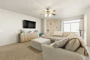 Carpeted living area featuring a ceiling fan and baseboards
