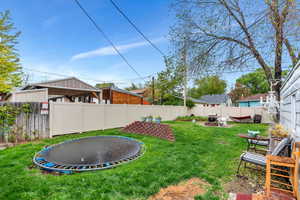 Fenced backyard featuring a trampoline, a fire pit, and a patio area