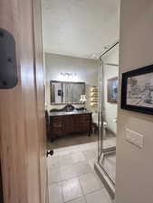 Full bathroom with vanity, light tile patterned floors, a textured ceiling, and a shower with door