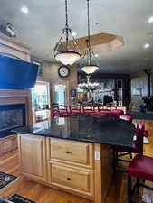 Kitchen featuring a fireplace, light wood-type flooring, pendant lighting, dark stone countertops, and light wood finish cabinets