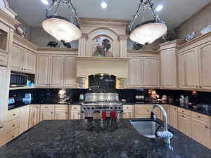 Kitchen with stainless steel appliances, dark stone countertops, light wood finish cabinets, decorative light fixtures, and tasteful backsplash