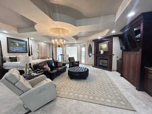 Living area with a chandelier, a premium fireplace, a raised ceiling, and light carpet