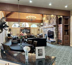 Carpeted dining area featuring beamed ceiling, a stone fireplace, hanging lights, and a textured ceiling