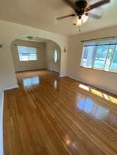 Unfurnished living room with light wood-style floors, a ceiling fan, plenty of natural light, and arched walkways