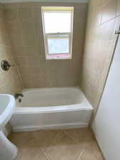 Full bath with light tile patterned floors and washtub / shower combination
