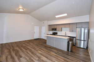 Kitchen featuring stainless steel appliances, light countertops, a kitchen island, open floor plan, and dark wood finished floors