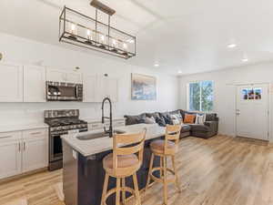 Kitchen with stainless steel appliances, open floor plan, an island with sink, light wood-type flooring, and a breakfast bar area