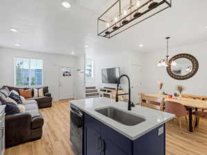 Kitchen featuring blue cabinets, open floor plan, light wood-style flooring, light stone counters, and dishwasher