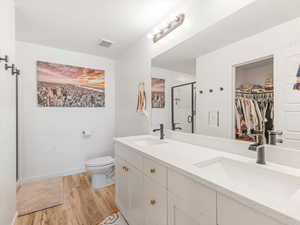 Full bathroom featuring a shower stall, a walk in closet, light wood-type flooring, and double vanity