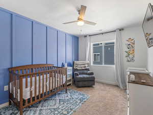 Bedroom with a nursery area, a decorative wall, light colored carpet, and ceiling fan