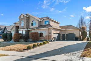Traditional-style home with stucco siding, stone siding, driveway, and an attached garage