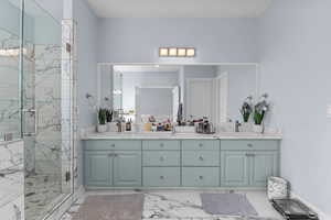 Bathroom with double vanity, a marble finish shower, and light marble finish flooring