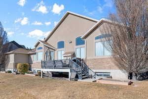 Back of property with a wooden deck, a lawn, stucco siding, and brick siding