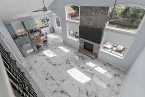 Living area featuring ceiling fan, vaulted ceiling, a fireplace, and light marble finish flooring