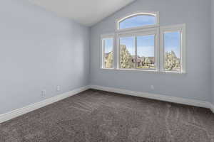 Spare room with dark carpet and lofted ceiling