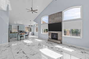 Living room featuring lofted ceiling, a chandelier, ceiling fan, light marble finish flooring, and a fireplace