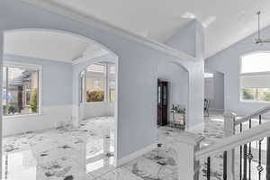 Corridor with lofted ceiling, arched walkways, healthy amount of natural light, and light marble finish flooring