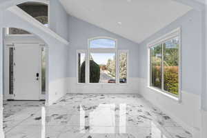 Foyer entrance with arched walkways, light marble finish floors, vaulted ceiling, plenty of natural light, and wainscoting