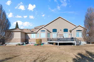 Rear view of house featuring a wooden deck, stucco siding, a lawn, and brick siding