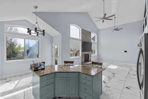 Kitchen with open floor plan, a high ceiling, a large fireplace, a ceiling fan, and dark stone counters