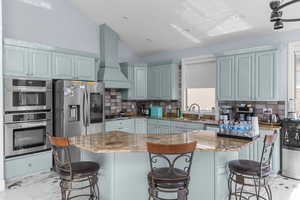 Kitchen with vaulted ceiling, light stone counters, stainless steel appliances, a breakfast bar area, and decorative backsplash