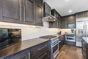 Kitchen with built in appliances, dark wood finish cabinetry, dark wood-style flooring, backsplash, and recessed lighting