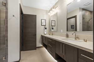 Bathroom featuring double vanity, tiled shower, and light tile patterned flooring