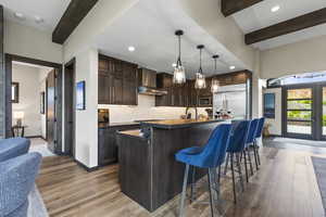 Kitchen with dark countertops, dark wood finish cabinets, a breakfast bar area, beamed ceiling, and hanging light fixtures