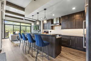 Kitchen featuring a breakfast bar area, decorative light fixtures, a center island with sink, beam ceiling, and dark wood finish cabinetry