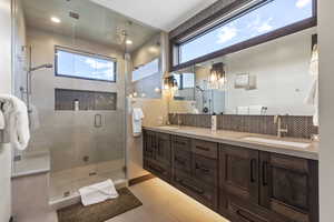 Bathroom with double vanity, a shower stall, backsplash, and light tile patterned floors