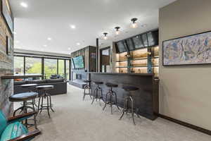 Indoor wet bar featuring recessed lighting, light colored carpet, dark countertops, and a large fireplace