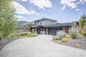 Contemporary home featuring driveway, stone siding, a mountain view, and a garage