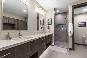Bathroom featuring double vanity, a tile shower, and light tile patterned flooring
