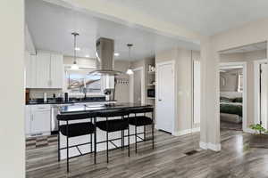 Kitchen with pendant lighting, a breakfast bar area, white cabinets, island range hood, and a center island