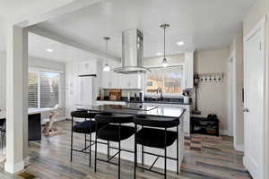 Open Kitchen with pendant lights, white cabinetry, island range hood, and light wood-style floors