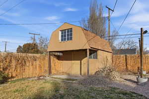 View of side of home featuring a gambrel roof, an outdoor structure, and a fenced backyard