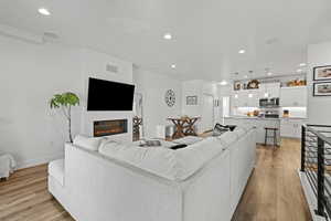 Living area with recessed lighting, light wood-style floors, and a glass covered fireplace