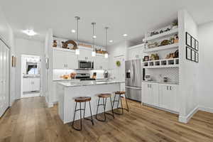 Kitchen featuring white cabinetry, hanging light fixtures, a breakfast bar area, light stone countertops, and stainless steel appliances