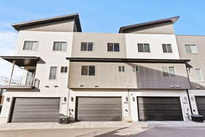 Back of house featuring an attached garage, a balcony, and stucco siding