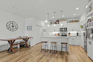Kitchen featuring white cabinets, pendant lighting, light stone countertops, and an island with sink