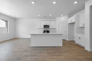 Kitchen with white cabinets, a center island with sink, light wood-style floors, stainless steel microwave, and recessed lighting