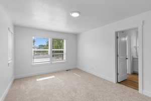 Empty room with light colored carpet and a textured ceiling