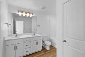 Full bathroom with double vanity, light wood finished floors, and shower / tub combination
